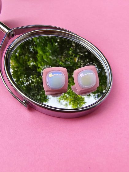 A product shot of the pink enamel square earrings, as seen on Karishma Tanna, reflected in a mirror.