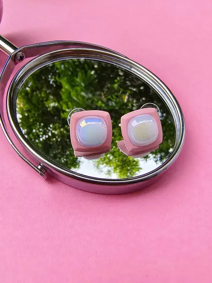 A product shot of the pink enamel square earrings, as seen on Karishma Tanna, reflected in a mirror.