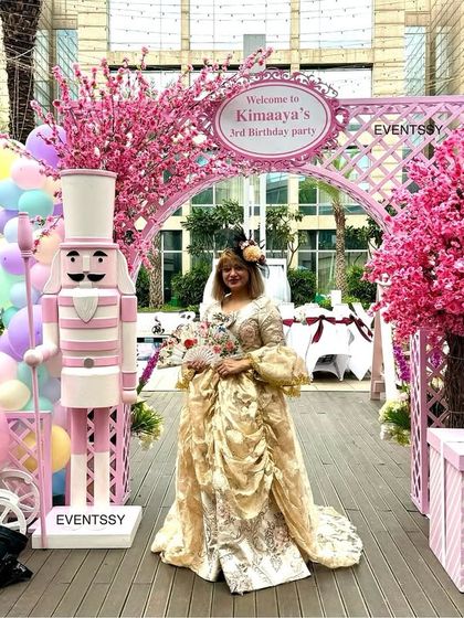 The entrance to the pastel carnival party, featuring a floral arch, nutcracker, and a costumed host.