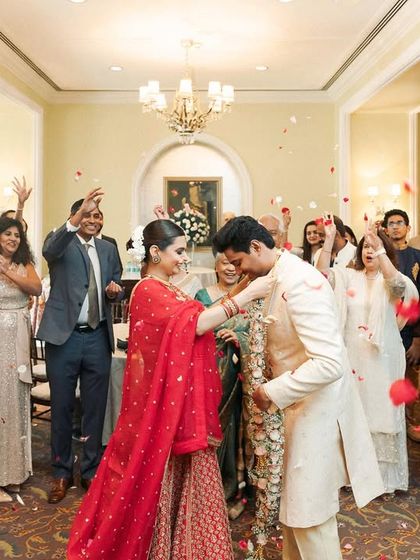 The Varmala exchange in an intimate indoor ceremony, with family cheering and showering the couple with petals. A moment of pure joy and celebration.