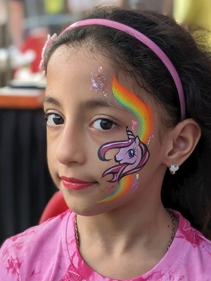 A close-up of a unicorn face paint with a rainbow background, perfect for a little girl's birthday.