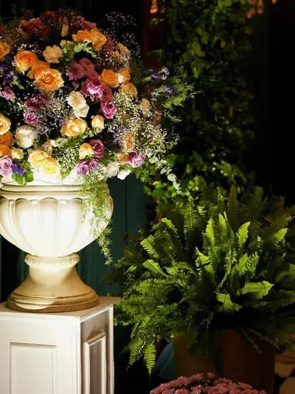 A large, elegant urn filled with a lush arrangement of colorful flowers, placed on a pedestal to serve as a statement decor piece.