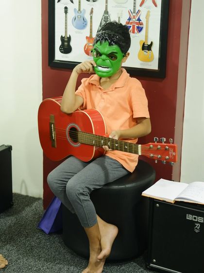 Even the Hulk needs to practice his guitar. A student in a Hulk mask with his red acoustic guitar during our Halloween event.