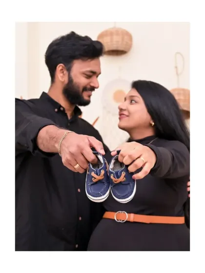 This is such a classic and sweet maternity pose. The couple holds up a tiny pair of baby shoes, a symbol of the little one they are so excited to meet. The Boho decor in the background adds a warm, stylish touch.