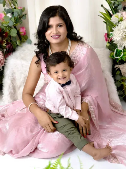 A mother in a pink saree smiles brightly with her little boy, who is dressed in a charming bow tie, during their studio session.