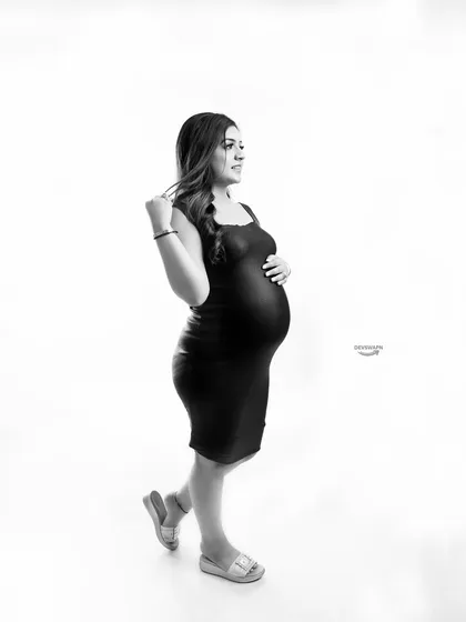 A timeless black and white portrait. The simple, fitted black dress and clean white background create a classic, high-contrast image that beautifully highlights the pregnancy silhouette.