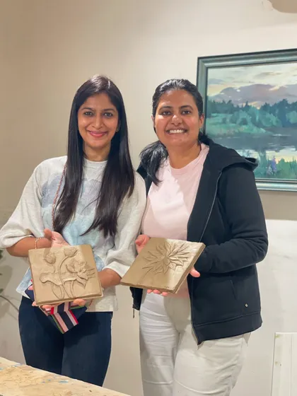 Two friends proudly holding the floral relief tiles they sculpted from clay. This is a great introductory project for anyone new to working with clay.