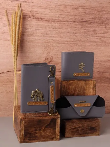 This coordinated set of personalized accessories in grey vegan leather includes a passport cover, wallet, keychain, and an eyewear case, each adorned with a custom nameplate and charm.