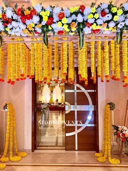 An entrance decorated with radiant yellow marigold garlands hanging from a floral canopy, creating a traditional and cheerful welcome for a wedding event.