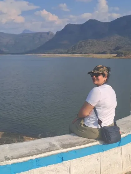 A traveler enjoying a peaceful moment overlooking the Aliyar Dam reservoir near Valparai. The calm water and distant mountains create a perfect scene for reflection.