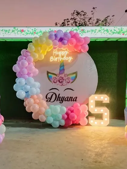 I love creating magical unicorn-themed parties. This outdoor setup for a 5th birthday includes a pastel rainbow balloon arch, unicorn cutouts, a personalized backdrop, and a light-up number '5' for a whimsical touch.