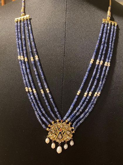 A full view of the iridescent peacock pendant necklace, displayed to show its length and the five elegant strands of sapphire beads interspersed with pearls.