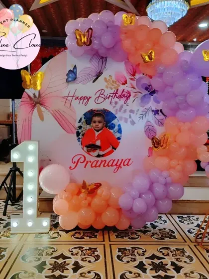A butterfly-themed first birthday with a custom photo backdrop, marquee number, and pastel balloon garland.