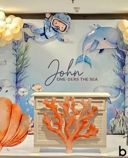 An 'Under the Sea' adventure for John's first birthday. This beautiful setup features a custom backdrop with whales and divers, pastel balloon arches, and charming seashell and coral props.