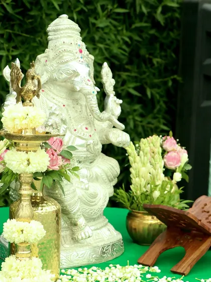 A silver Ganesha idol placed with a traditional lamp (diya) and fresh flowers, creating a sacred corner to bless the Haldi ceremony.