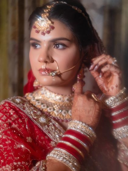 A close-up bridal portrait focusing on the details of her nath, jewelry, and the groom's name written in her mehndi.
