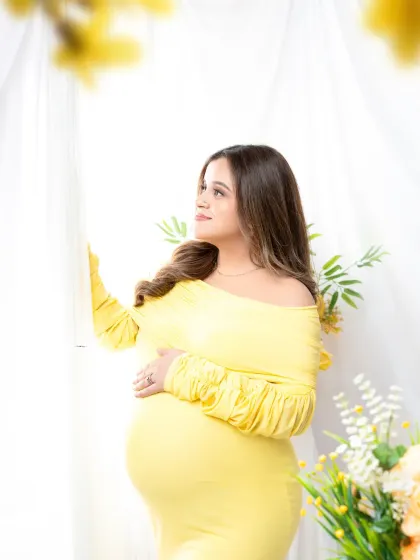 Looking towards the future. This hopeful portrait captures the mother-to-be in a bright yellow gown, gazing out a window surrounded by matching flowers.