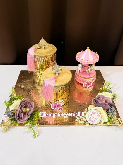A truly luxurious baby girl hamper featuring ornate golden jars with pink tassels and a musical carousel centerpiece.