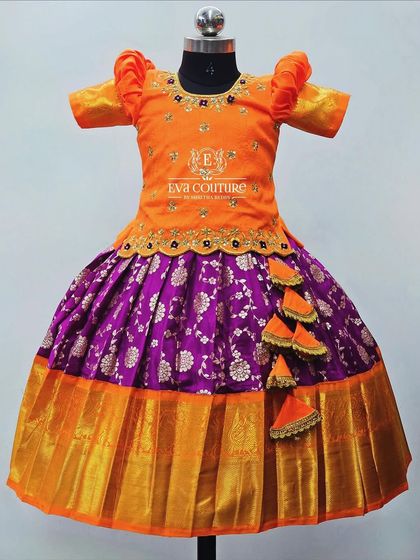 A bright orange and purple Banarasi lehenga. The blouse has a scalloped peplum, and the skirt has a silver floral brocade pattern.