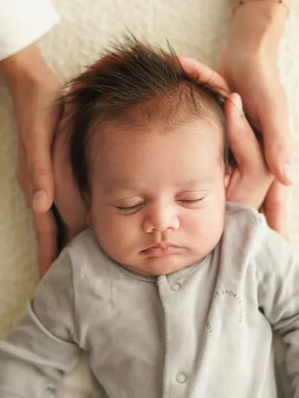 Another angle of parents' hands cradling their baby's head, focusing on the newborn's peaceful, sleeping face.