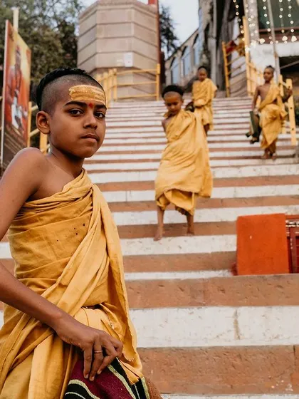 A young Batuk, or student monk, looks directly at the camera as he descends the steps of a ghat. His confident gaze offers a glimpse into the future generation of Varanasi's spiritual guardians.