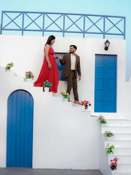 A fairytale moment on the steps of a beautiful Santorini-style building. The groom helps his bride-to-be, dressed in a flowing red gown, creating a classic and romantic cinematic shot.