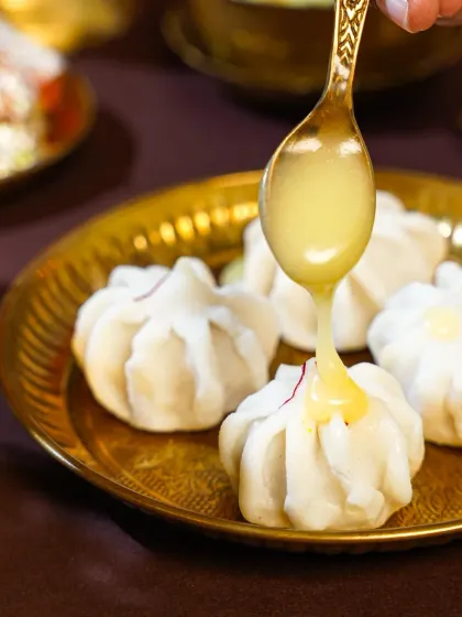 A decadent stream of golden ghee being poured over delicate, steamed Modaks. This action shot is both luxurious and traditional, capturing a key moment in enjoying this festive sweet.