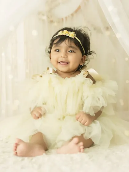 A happy baby girl in a yellow tulle dress, surrounded by a dreamy, light-filled setup.