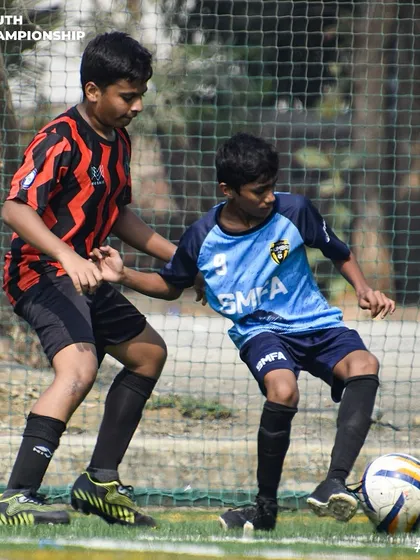 An intense one on one battle on the turf, as our player in the red and black kit shields the ball from the opposition.