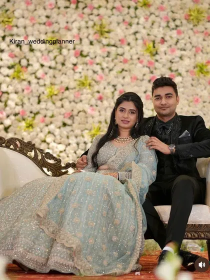 A couple seated against a dense wall of white and light pink flowers. This classic and elegant floral backdrop is timeless and perfect for reception photos.