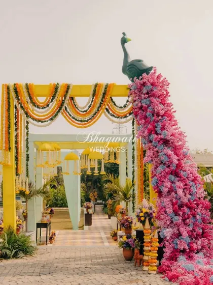 The full entrance view of a 'Phoolon Ki Holi' haldi ceremony. The archway is decorated with marigold garlands and a stunning floral peacock, welcoming guests to a vibrant celebration.