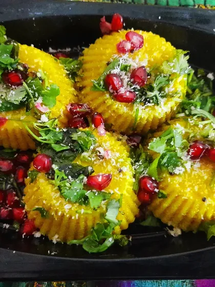 A fun and modern take on a classic: Nylon Khaman presented as bite-sized savory cupcakes. They are garnished with fresh coriander, coconut, and pomegranate jewels.