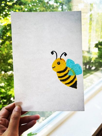 A hand holding up the completed honey bee drawing, showing the charming result of a guided drawing session for kids.