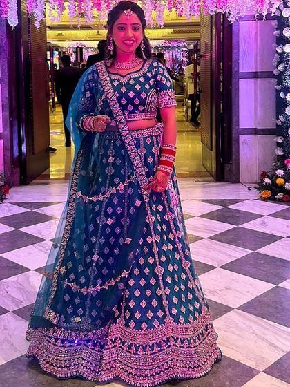 A beautiful bride wearing a royal blue velvet lehenga with pink embroidery for one of her wedding functions. The color combination is striking and perfect for an evening event.