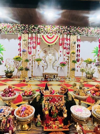 A grand Seemantham setup, showcasing the main stage, ornate chair, and an extensive display of traditional offerings. The backdrop features red and white floral hangings for a classic look.