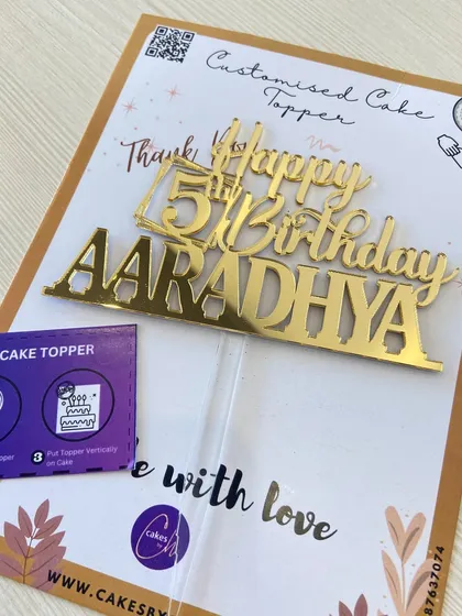 This "Happy 5th Birthday AARADHYA" topper is shown with its packaging and instructions, so you can see exactly how it will arrive.