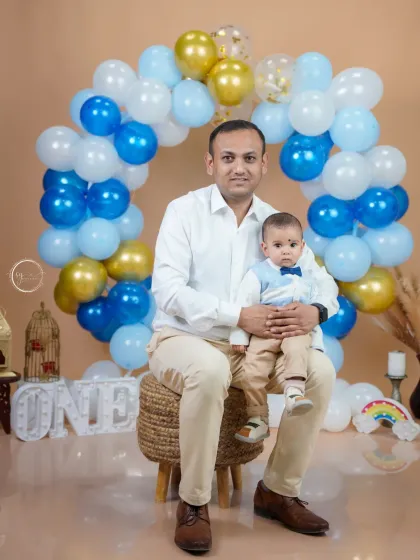 A sweet father and son portrait during a first birthday celebration. The festive balloon setup in the background marks the special occasion, while the focus remains on their connection.