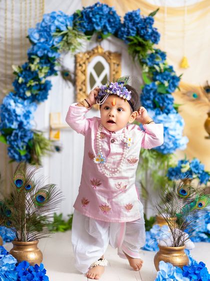 A playful moment as this little Krishna adjusts his floral crown. These candid shots are often the most charming and memorable.