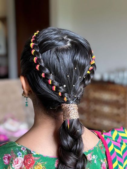 A unique and colorful braided ponytail. This style features a crown braid and a lower braid woven with bright pink and yellow threads, perfect for a vibrant Mehendi or Navratri look.