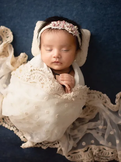 Wrapped in delicate lace. This portrait emphasizes texture and elegance, with a beautifully detailed wrap and headband against a deep blue backdrop.