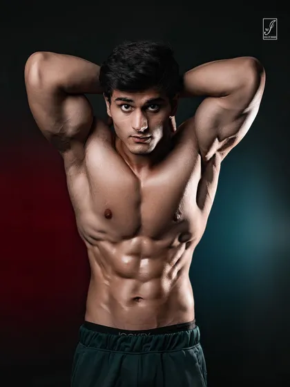A modern athletic portrait using dual-tone red and blue lighting to add mood and dimension. The focus is on sharp abdominal definition and a confident, direct-to-camera pose for a high-impact fitness portfolio shot.