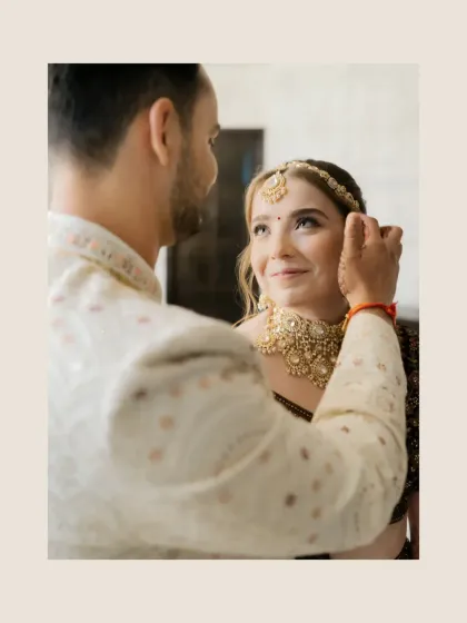 A tender moment where the groom gently adjusts the bride's maang tikka, a small gesture full of love.