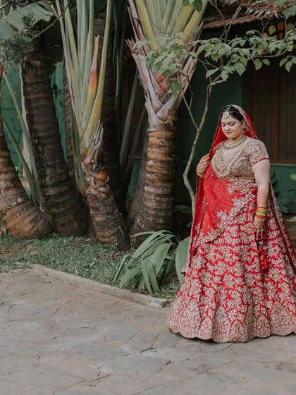 The bride in her red lehenga, posing against the backdrop of tropical plants.