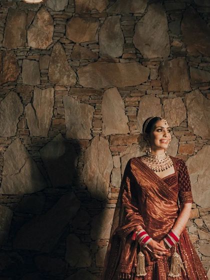 A striking portrait of the bride against a stone wall, the dramatic lighting highlighting her and her beautiful lehenga.