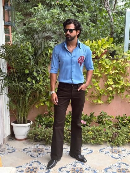 Our hand-painted blue shirt, styled with dark flared trousers in a lush garden setting. It's the ideal look for a stylish brunch or daytime gathering.