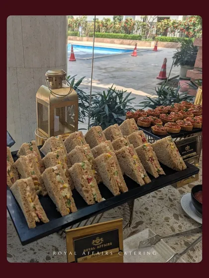This poolside buffet setup includes classic club sandwiches and mini bruschetta, perfect for a relaxed daytime event. The food is arranged on modern black platters and tiered stands for easy access.