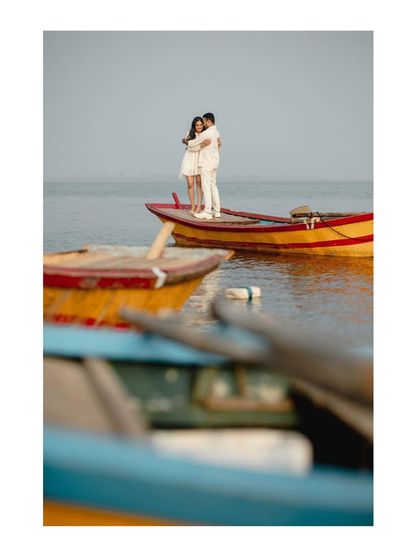 A beautifully composed shot of the couple embracing on a boat, framed by other colorful boats in the foreground. It creates a sense of depth and context.