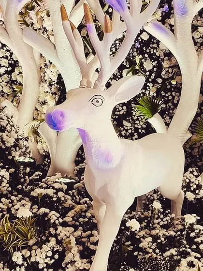 A whimsical white deer prop, nestled among a bed of white flowers as part of a larger divine-themed installation. These artistic elements help to build a narrative and create a magical atmosphere.