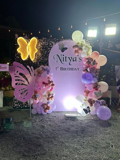 An outdoor butterfly-themed party at night. This setup uses a shimmer wall, a personalized arched backdrop, and illuminated butterfly props to create a magical evening ambiance.