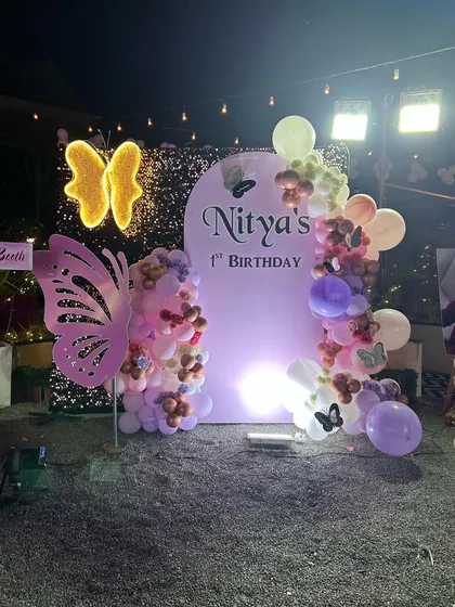 An outdoor butterfly-themed party at night. This setup uses a shimmer wall, a personalized arched backdrop, and illuminated butterfly props to create a magical evening ambiance.